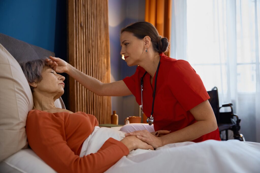 Female caregiver measuring temperature touching forehead of old woman