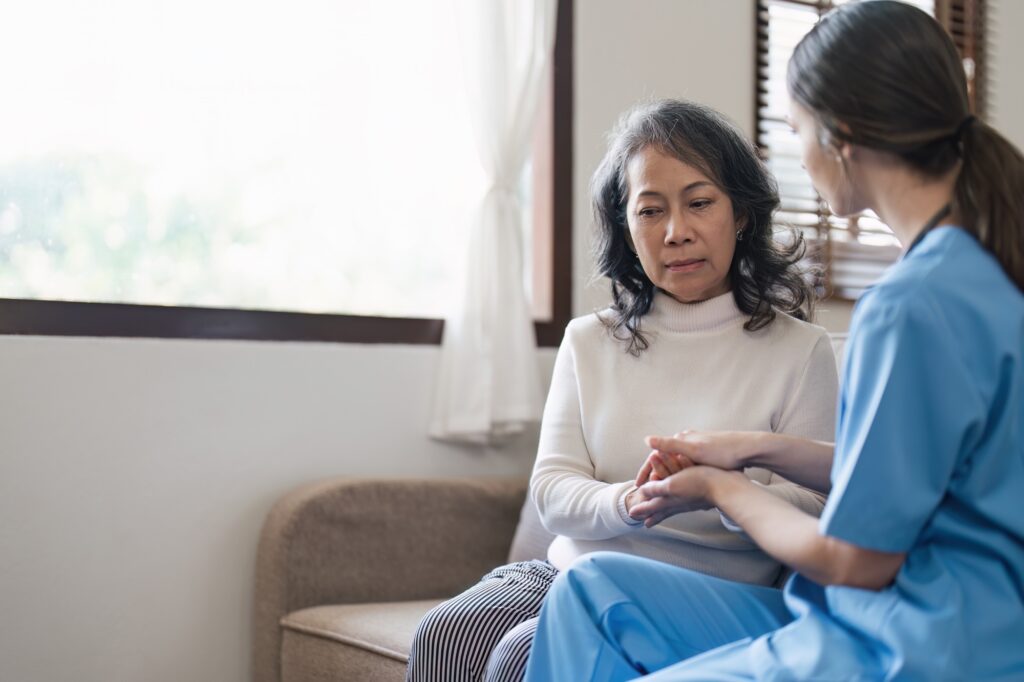 Nurse or caregiver comforting senior woman on sofa in home. Healthcare and emotional support